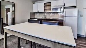 A modern kitchen with white cabinets, a microwave, a refrigerator, and a dining table with chairs. - 1BR Queen Suite w/ Hot Breakfast, Workspace & Pool (Albuquerque)