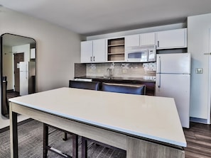 A modern kitchen with white cabinets, a microwave, a refrigerator, and a dining table with chairs.