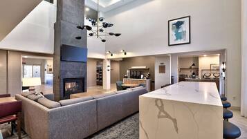 A modern living room with a fireplace, a large sofa, a dining area, and a kitchen in the background.