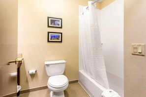 Un baño con inodoro, ducha con cortina blanca y dos cuadros en la pared.