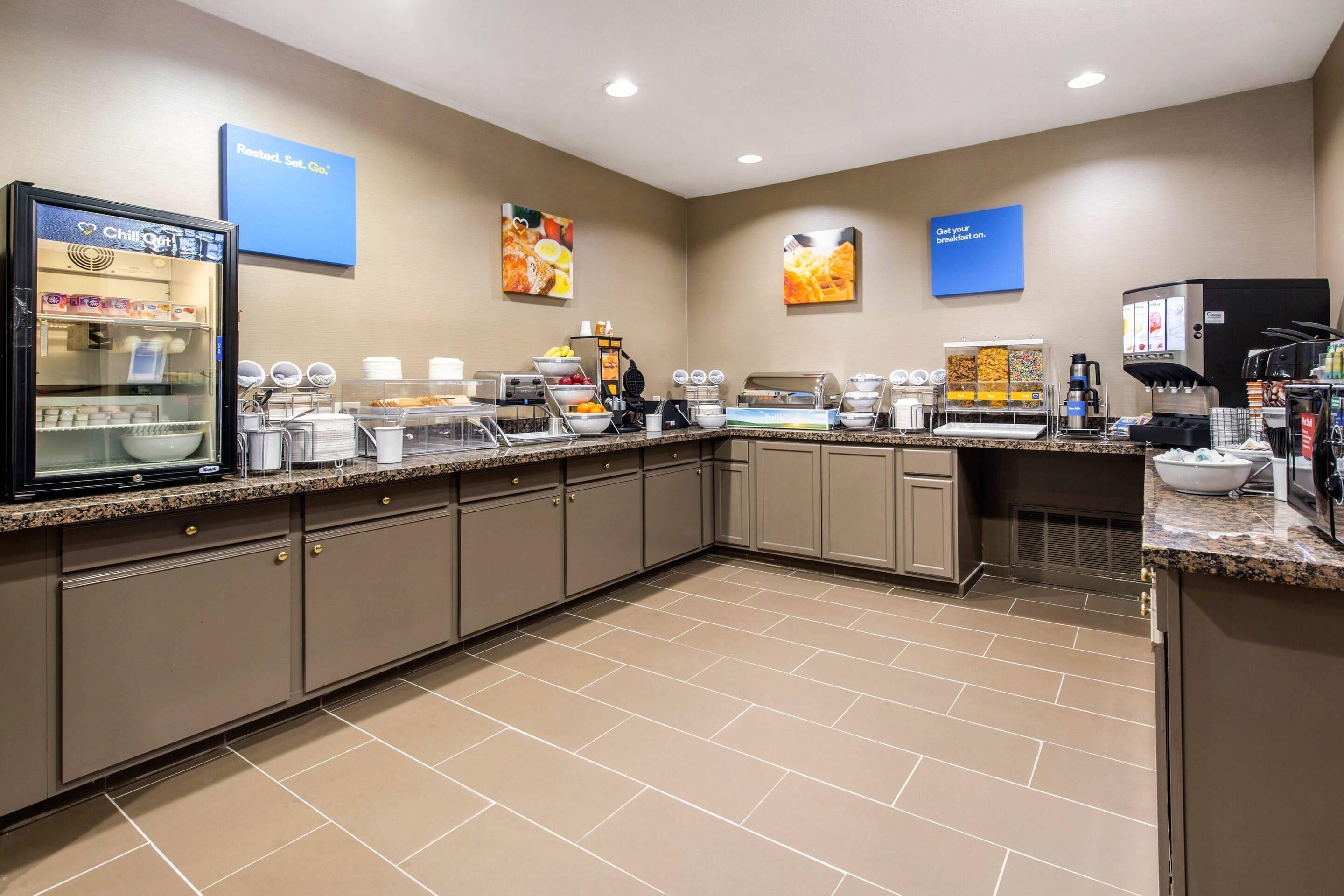 A hotel breakfast area with a self-serve station, a refrigerator, and a coffee machine.