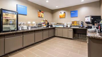 A hotel breakfast area with a self-serve station, a refrigerator, and a coffee machine.