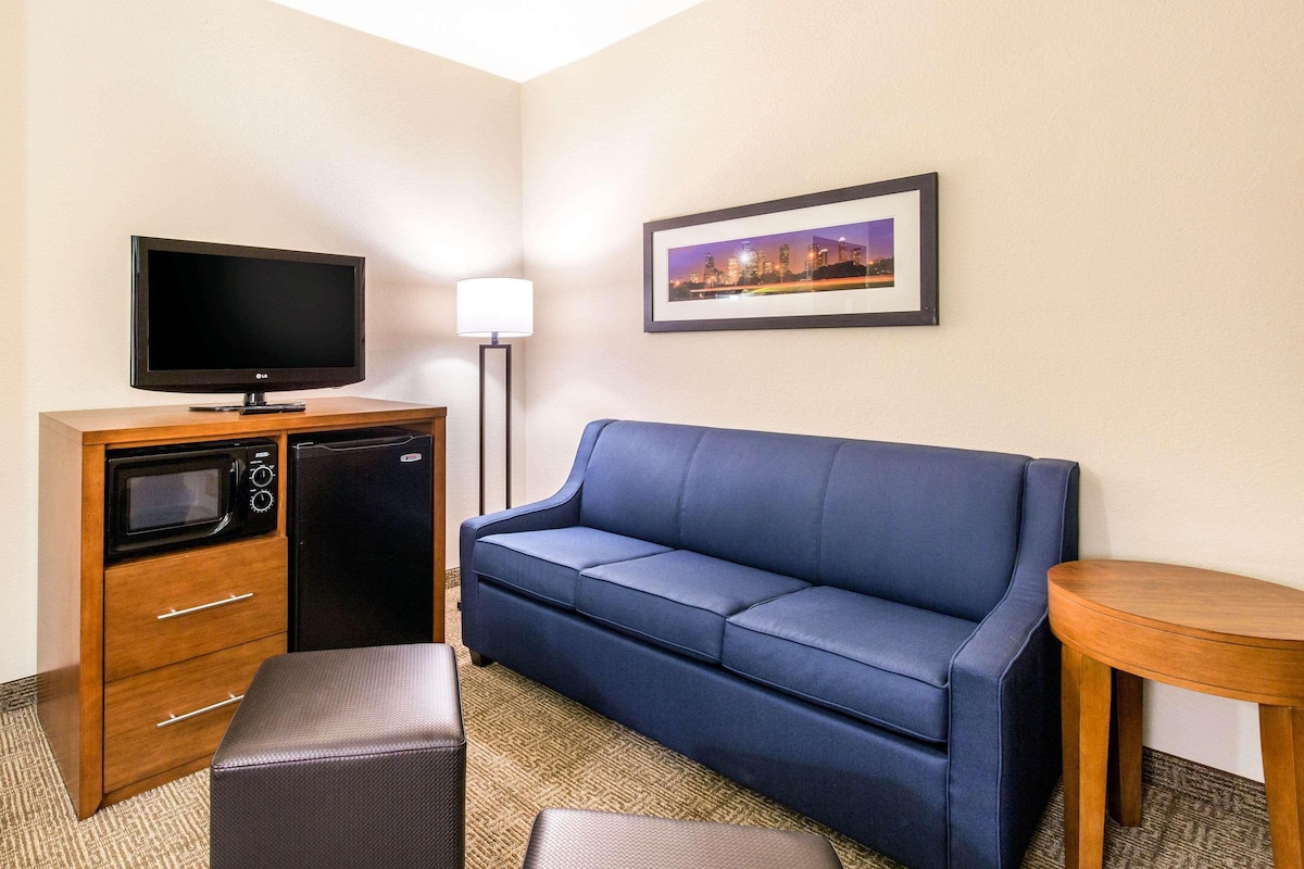 A hotel room with a flat-screen TV, a microwave, a refrigerator, a blue sofa, a small round table, and a framed picture on the wall.
