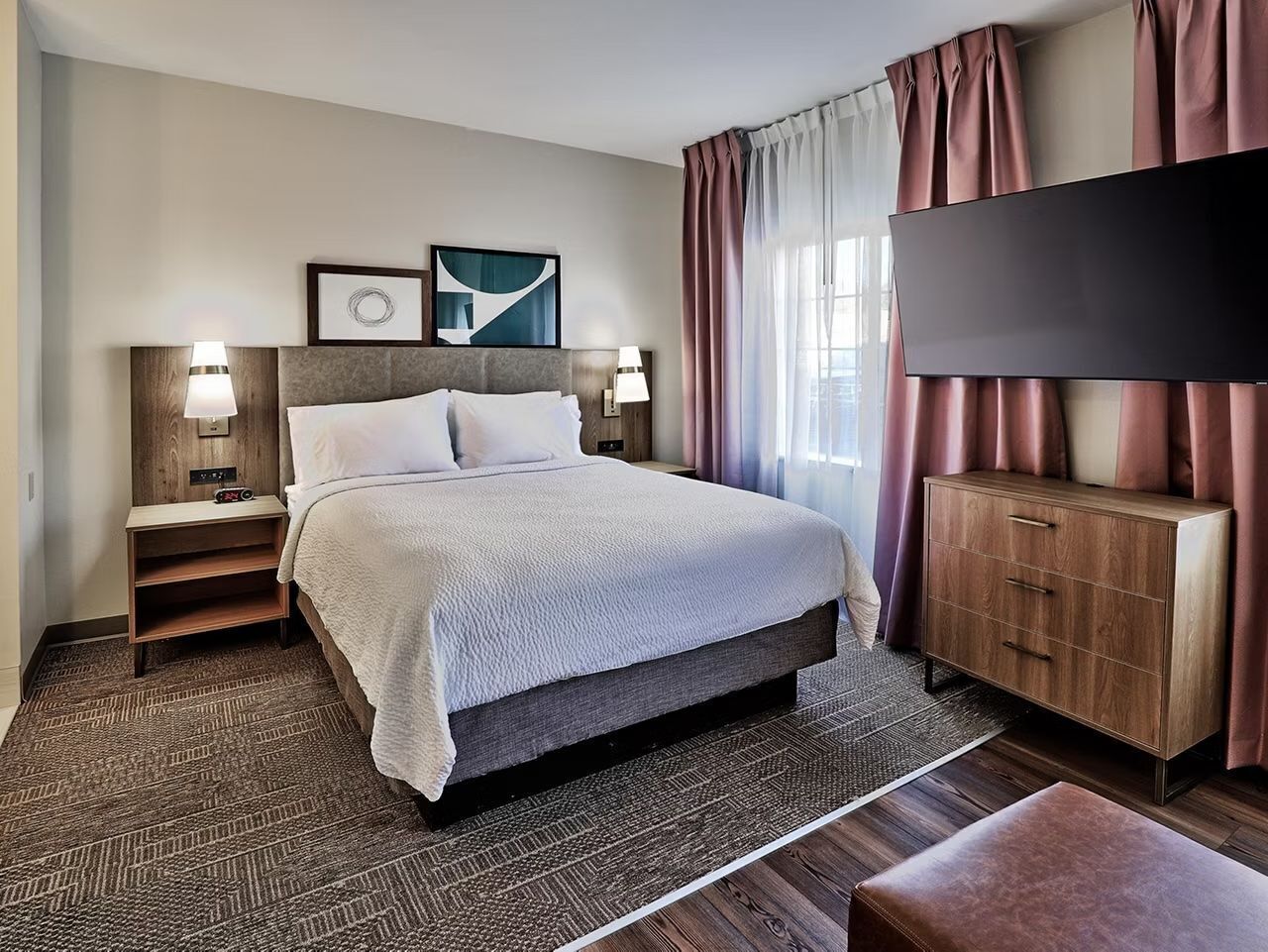 A hotel room with a bed, nightstands, a TV, and a wooden cabinet.