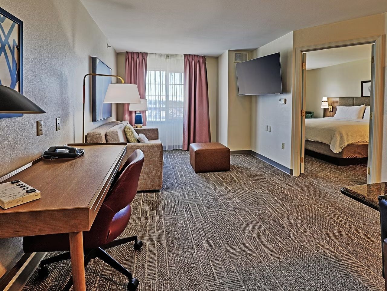 A hotel room with a wooden desk, a sofa, a TV, and a bed.