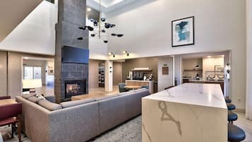 A modern living room with a fireplace, a large sofa, a dining area, and a kitchen in the background.