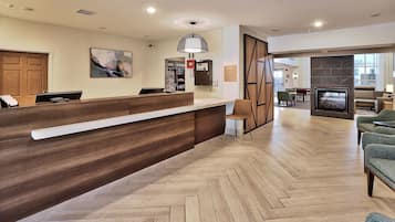 A hotel reception area with a wooden reception desk, a painting on the wall, and a herringbone patterned floor.