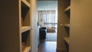 Ein schmaler Flur mit eingebauten Regalen an beiden Seiten, der zu einem Zimmer mit Bett und Fenster führt.