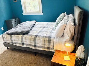 Un dormitorio con cama, mesita de noche, lámpara y ventana.