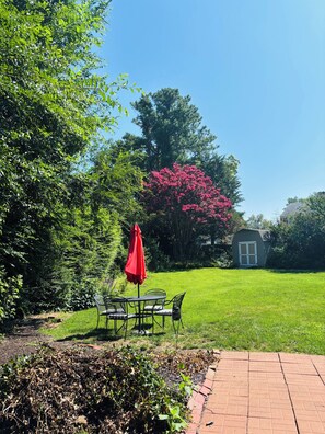 A garden with a patio table and chairs, a red umbrella, and a brick pathway. - Cozy Comfy Pet Friendly House in a Quiet Neighborhood  (Wilmington)