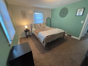 A bedroom with a bed, a nightstand, a window with blinds, and a wall with a decorative plate. - Cozy Comfy Pet Friendly House in a Quiet Neighborhood  (Wilmington)