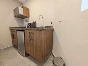 Eine kompakte Küche mit integriertem Geschirrspüler, einem Edelstahl-Kühlschrank, Holzschränken und einer Arbeitsplatte aus Granit, sowie einem einzelnen Wasserhahn.