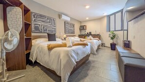 Habitació d'hotel amb tres llits, un ventilador, una televisió i un cartell informatiu de la ubicació.