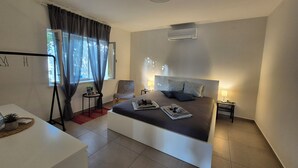 Una camera d'albergo moderna con un letto, comodini, una sedia, un tavolino con una pianta e una finestra con tende.