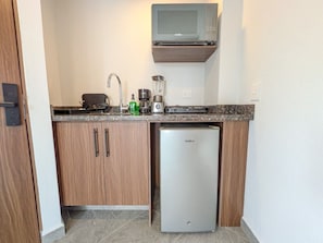 Eine kleine Küchenzeile mit Mikrowelle, Kaffeemaschine, Mixer und einem kleinen Kühlschrank.