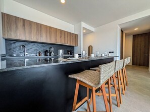 Een moderne keuken met een zwart aanrecht, houten barstoelen en een houten kast.