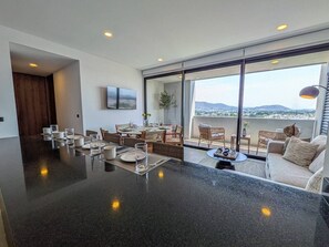 Cocina moderna con una isla grande, comedor con sillas y mesa, y un balcón con asientos.