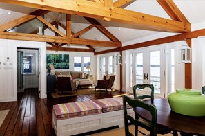 Ein geräumiges Zimmer mit Holzbalkendecke, einem Esstisch, einer Bank und Blick ins Freie.
