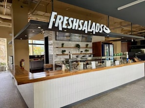Modernissa sisustuksessa oleva tiski, jonka yläpuolella on kyltti, jossa lukee ”FRESHSALADS”. Tiskissä on laattapintainen seinäosa ja puinen työtaso.