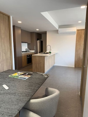 Een moderne keuken met een centraal eiland, een eethoek met een tafel en stoelen, en uitzicht op de woonkamer.