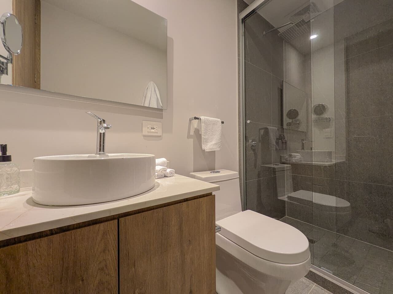 A modern bathroom with a round sink, a toilet, and a glass-enclosed shower.