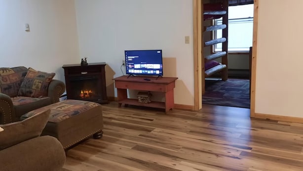 Ein Wohnzimmer mit Sofa, Hocker, Kamin, Fernseher und Lampe.