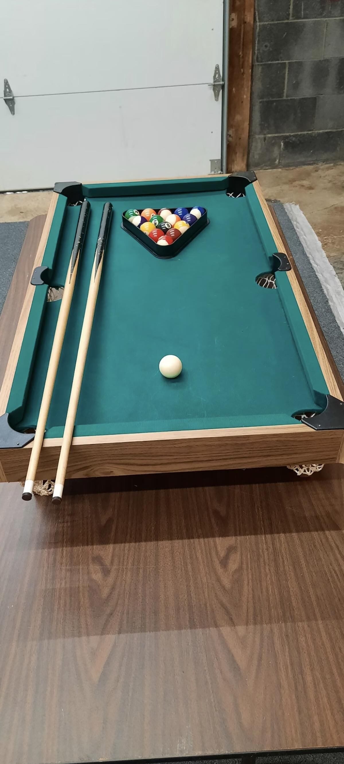 A pool table with a cue stick, billiard balls, and a white ball on the table.