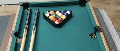 A pool table with a cue stick, billiard balls, and a white ball on the table.