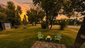 A backyard with a paved patio, two green Adirondack chairs, a small table, and a shed. - Charming Moore Home. Pet Friendly, Spacious & Comfortable for Families (Moore)