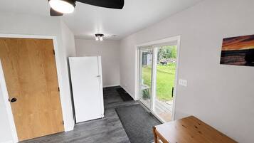 A hallway with a wooden door, a white refrigerator, a ceiling fan, and a view through glass doors to an outdoor area.