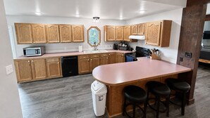 A modern kitchen with wooden cabinets, a central island with stools, a microwave, and a dishwasher. - Charming Moore Home. Pet Friendly, Spacious & Comfortable for Families (Moore)