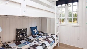 Camera con letto a castello, copripiumino trapuntato, finestra vista e pareti di legno bianco.
