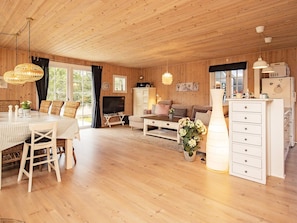 Ein Zimmer mit Holzwandverkleidung, einem Esstisch, einer Couch, einem Fernseher und einem weißen Schrank.