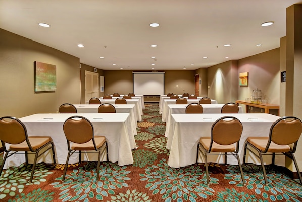 A conference room with multiple tables and chairs, a projector screen, and a carpeted floor.