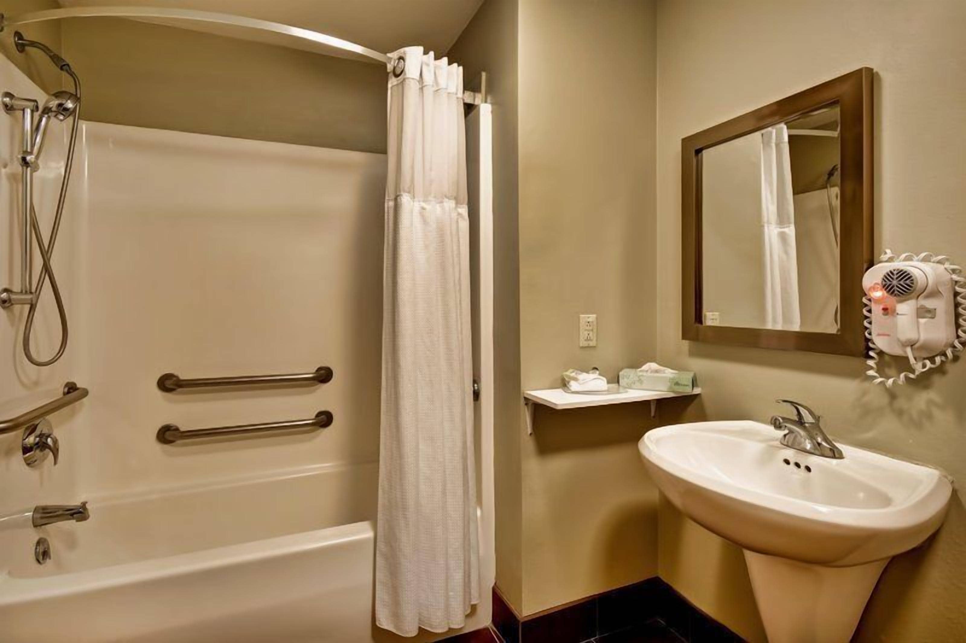 A bathroom with a bathtub, shower, and sink, equipped with a hairdryer and a mirror.
