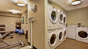 Academia com equipamentos de ginástica e área de lavanderia com várias máquinas de lavar.