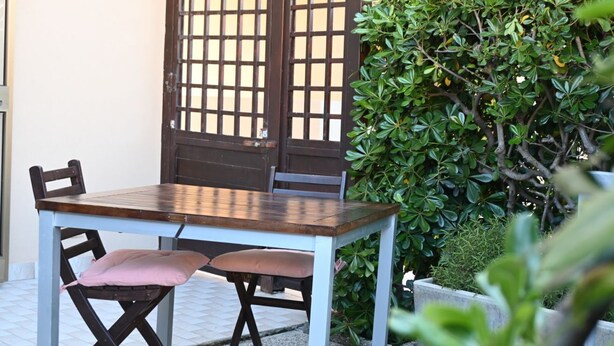 A dining table with chairs, a wooden partition, and a green hedge. - SE273 – Senigallia, studio apartment near the sea (Senigallia)