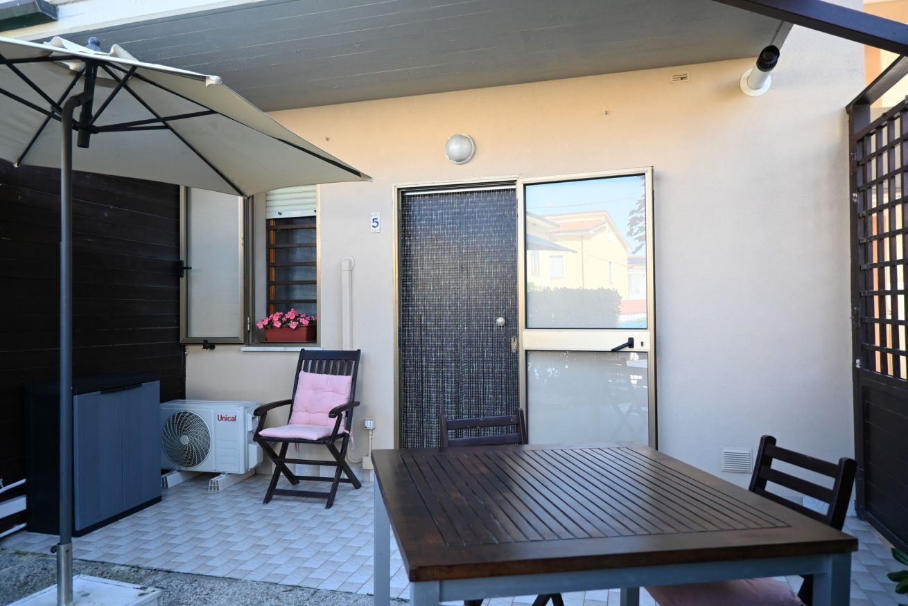 A patio with a table and chairs, an air conditioning unit, a window with a view, and a door with a number.