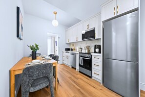 A modern kitchen with white cabinets, stainless steel appliances, and a wooden dining table. - The Gerrard Match Stay w Private Patio (Toronto)