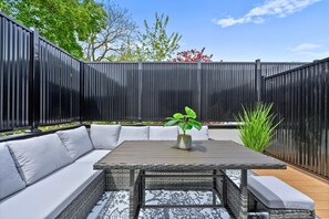 Une terrasse avec une table et un canapé, entourée d’une clôture noire.