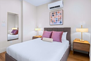 Une chambre d’hôtel comprenant un lit, deux tables de chevet avec des lampes, un climatiseur fixé au mur et une œuvre d’art encadrée.