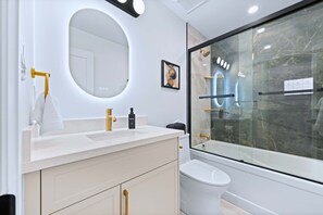 A modern bathroom with a white vanity, gold fixtures, a large mirror, and a glass-enclosed shower. - The Gerrard Private Patio Near Riverdale Park (Toronto)