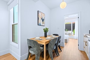 A dining area with a wooden table set for four, grey upholstered chairs, a potted plant, and a framed abstract painting on the wall. - The Gerrard Match Stay w Private Patio (Toronto)