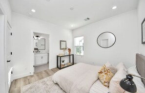 Un dormitorio moderno con cama, mesita de noche, lámpara y vista al baño.