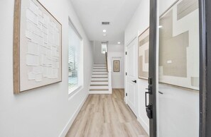 A hallway with wooden flooring, white walls, and framed artwork. - Elysian Estates Modern Townhome 2BR (Houston)