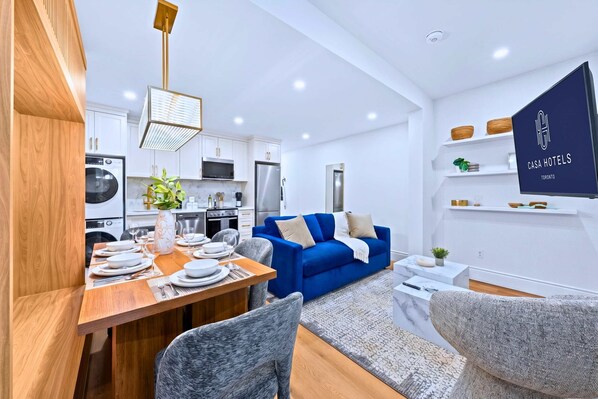 Une cuisine moderne avec des meubles blancs, un canapé bleu et un coin repas avec une table en bois, mise pour quatre personnes.