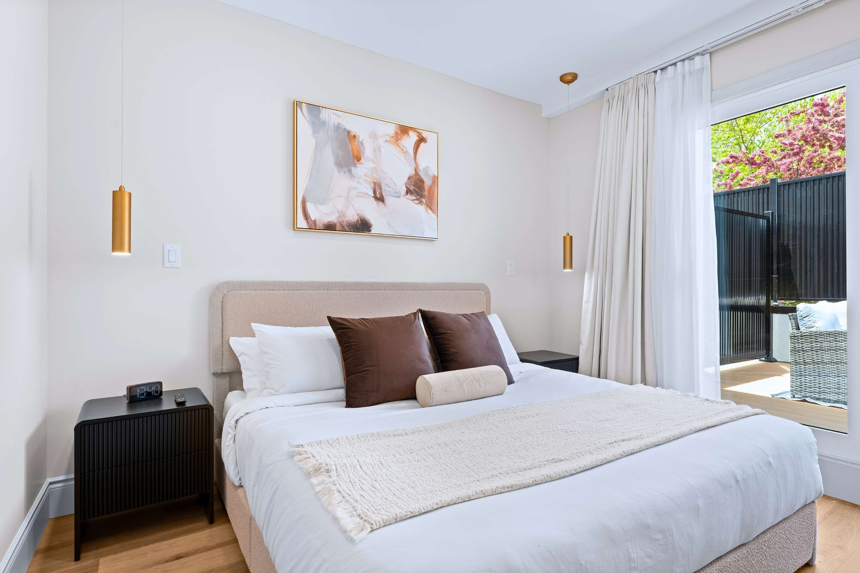 Een slaapkamer met een bed, nachtkastje, schilderij en uitzicht op de omgeving.