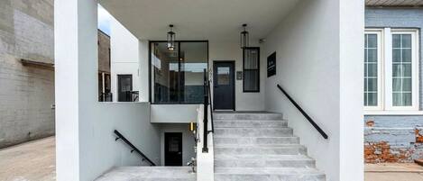 A modern building entrance with a staircase, a glass door, and a metal railing.
