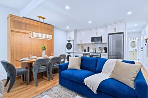 Une cuisine moderne avec des meubles blancs, un réfrigérateur en acier inoxydable et un coin repas comprenant une table en bois et des chaises grises.