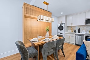 Una cocina moderna con armarios blancos, una mesa de comedor de madera preparada para cuatro personas y un sofá azul.